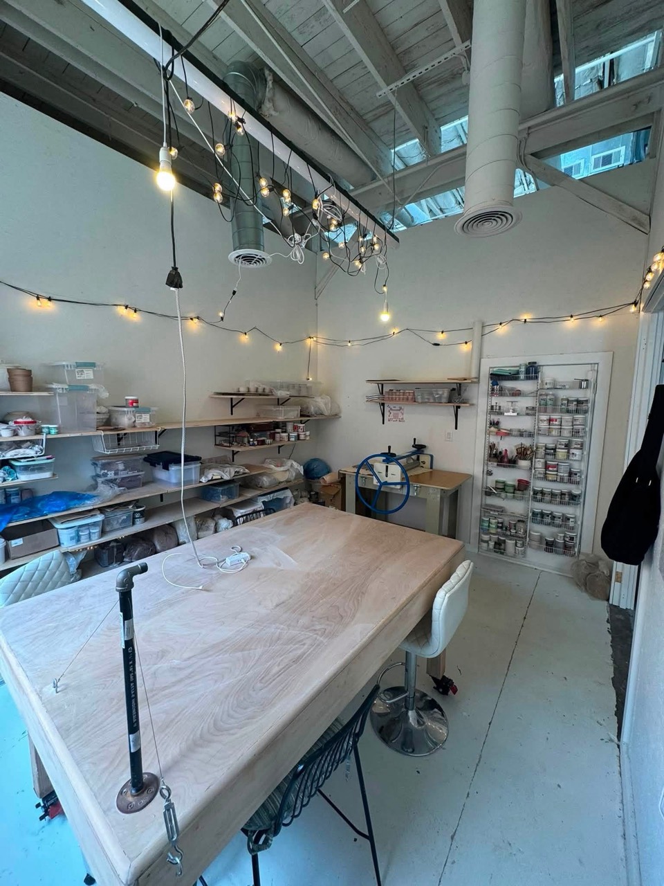 Shared ceramics worktable surrounded by material storage and a wall of studio glazes